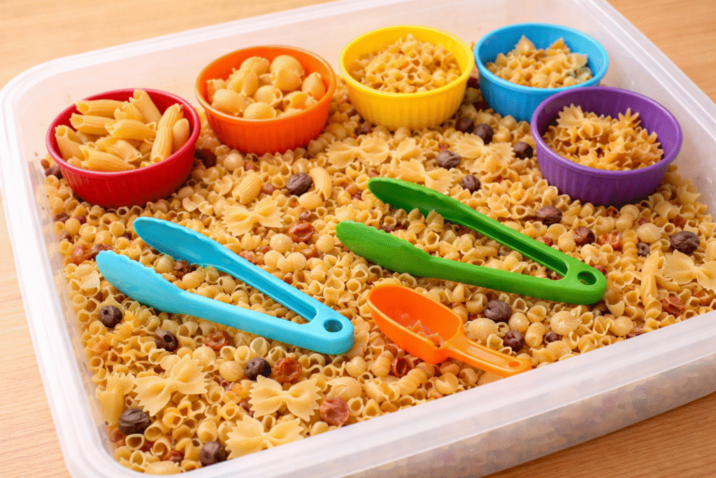 easy sensory bin of dried pasta, tongs, scoops, and bowls for sorting
