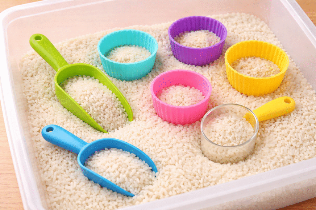 easy sensory bin of white rice, scoops, and muffin papers
